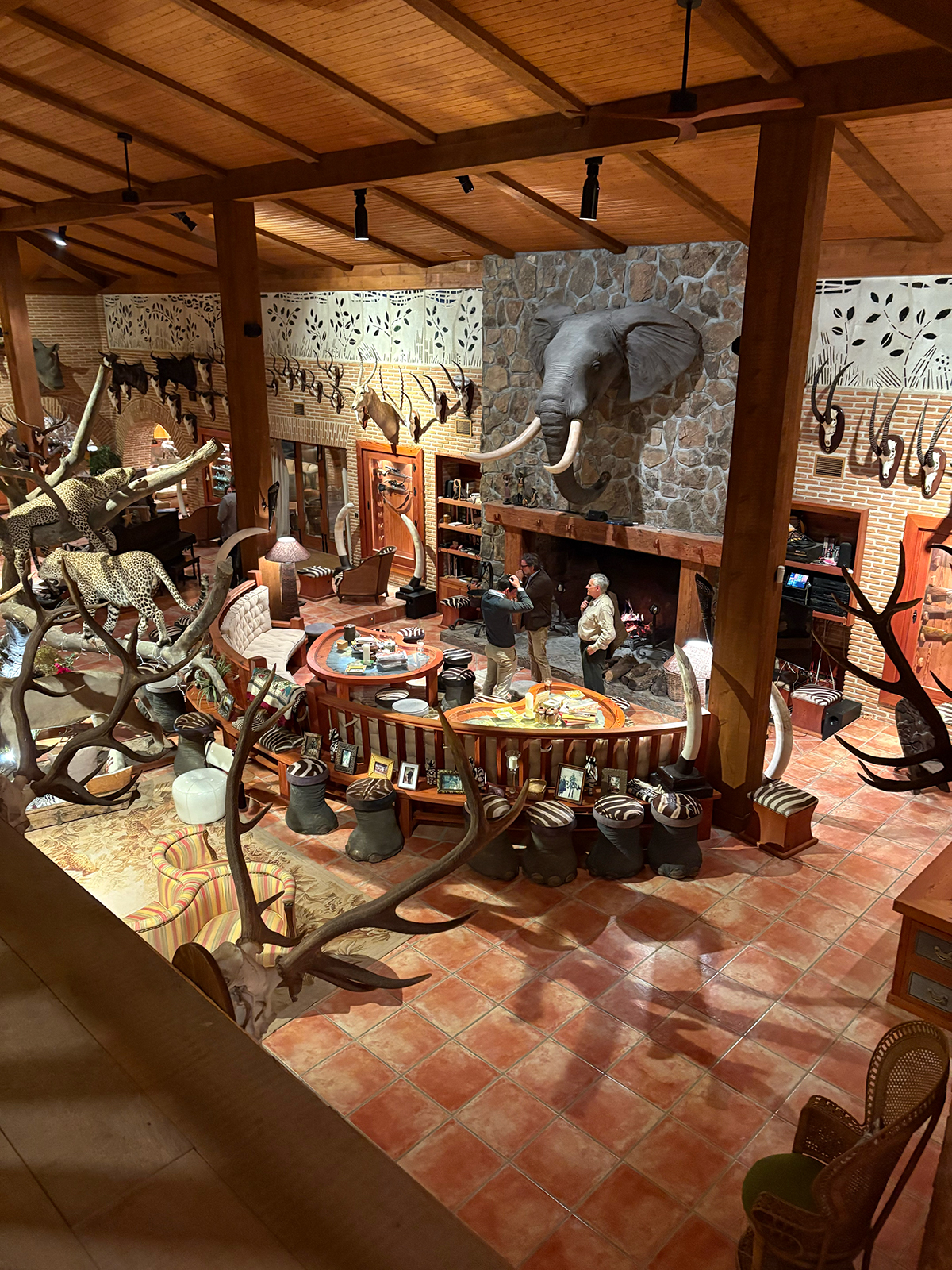 Interior of a luxurious hunting lodge featuring taxidermy displays, including an elephant head and various animal horns, with a cozy seating area and a central table set for guests, reflecting the upscale environment of a premier wingshooting estate in Spain.