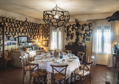 Dining room at El Despeñadero Lodge featuring a round table set for a meal, adorned with hunting trophies on the walls, showcasing rustic decor and a warm ambiance for post-hunt gatherings.