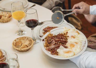 Plate of bacon and fried eggs being served at a dining table with wine glasses and orange juice, highlighting the culinary experience at El Despeñadero Lodge.