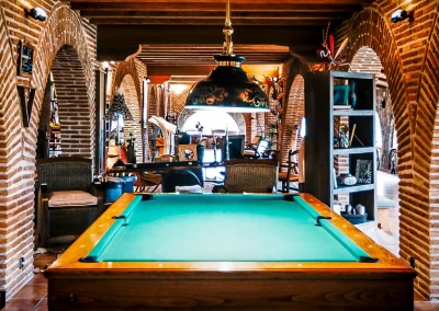 Interior of El Despeñadero lodge featuring a billiards table, rustic brick arches, and cozy seating areas, reflecting the inviting atmosphere for hunters after a day of shooting adventures.