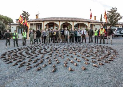 Group of hunters and staff at El Despeñadero Lodge posing with a large display of harvested red-legged partridges, showcasing the successful hunting experience in a scenic Spanish setting.