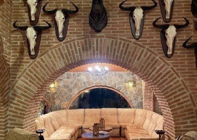 Cozy lounge area in El Despeñadero Lodge featuring a curved leather sofa, rustic decor, and mounted animal skulls on brick walls, reflecting the hunting heritage and ambiance of the estate.