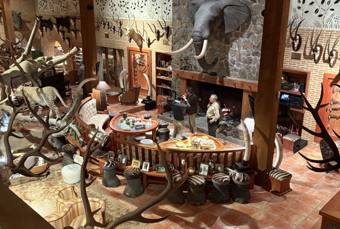 Interior of El Despeñadero Lodge featuring taxidermy displays, rustic furnishings, and guests interacting by a cozy fireplace, showcasing the hunting heritage of the estate.