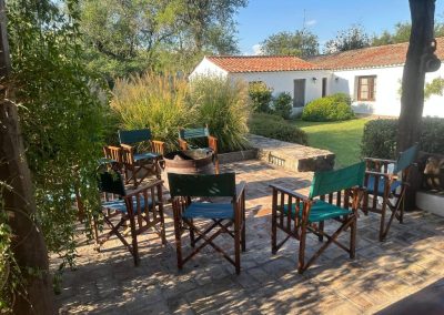 Outdoor seating area at El Palomar Hunting Lodge in Argentina, featuring wooden chairs and a tranquil garden setting, ideal for relaxing after a day of wingshooting adventures.
