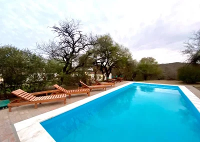 Swimming pool with wooden loungers and surrounding trees at El Palomar Hunting Lodge in Argentina.