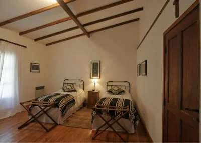 Cozy twin-bedded room at El Palomar Hunting Lodge, featuring traditional Argentine decor, wooden beams, and warm lighting, ideal for hunters seeking comfort and relaxation.