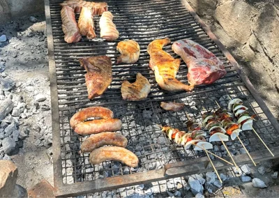 Grilled meats including sausages, ribs, and skewers on a barbecue grill, representing traditional Argentine cuisine at El Palomar Hunting Lodge in Argentina.