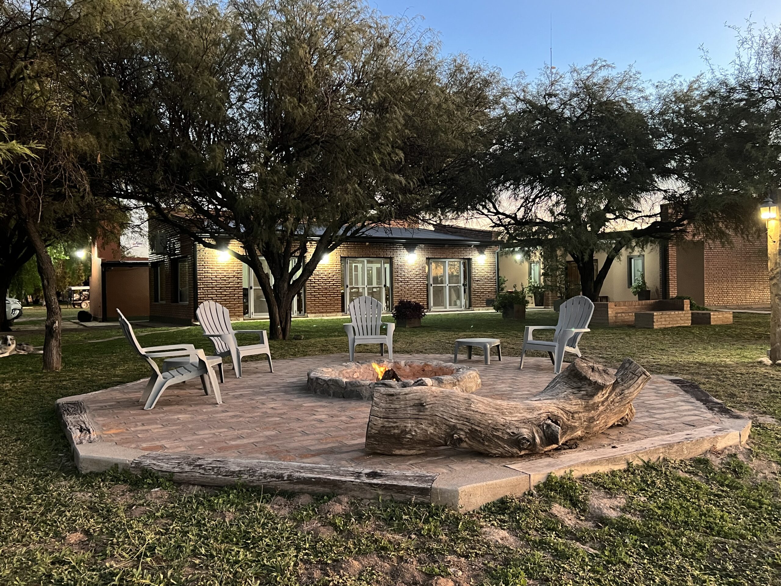 Cozy outdoor fire pit area with wooden seating, surrounded by trees, at Estancia La Emilia, a premier hunting destination in Argentina.