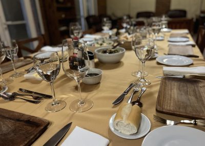 Dining table set for traditional Argentine asado at Estancia La Emilia, featuring wine glasses, plates, and a variety of dishes, emphasizing the cultural experience after a day of pigeon and dove hunting.