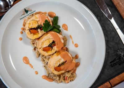 Dish of rolled chicken with vegetables on a bed of risotto, garnished with parsley and sauce, showcasing culinary offerings from a hunting lodge experience.