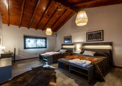 Cozy lodge room at Estancia Las Palomas featuring two beds, wooden ceiling, and warm lighting, reflecting traditional Argentine hospitality for hunting guests.