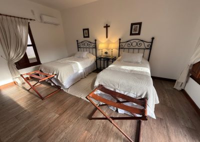 Cozy twin bedroom with wooden floors, decorative cross, and elegant bedding in Las Tapias dove hunting retreat, emphasizing luxury and comfort.