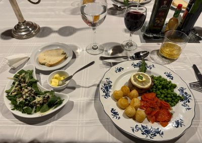 Elegant dining setup featuring a plate of gourmet food with a meat dish, vegetables, and potatoes, accompanied by a fresh salad, bread, and beverages including red wine and water, on a white tablecloth at Las Tapias dove hunting retreat.