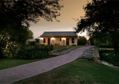 Lodge exterior at Las Vertientes, Argentina, featuring a welcoming pathway, illuminated building, and lush greenery, reflecting the intimate atmosphere for wingshooting adventures.