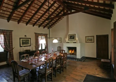 Cozy dining area in Las Vertientes lodge, featuring a large wooden table, rustic decor, and a fireplace, reflecting the intimate atmosphere for small groups in Córdoba, Argentina.