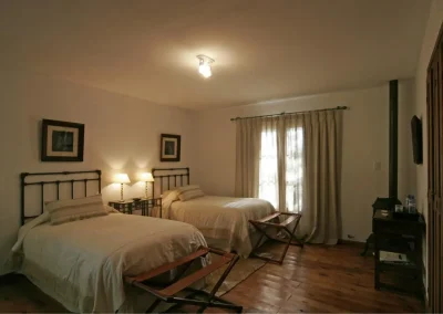 Comfortable twin bedroom in Las Vertientes lodge, featuring natural light, wooden flooring, and cozy decor, ideal for relaxing after wingshooting adventures in Córdoba, Argentina.