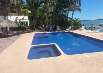Swimming pool at La Marina Del Río lodge surrounded by palm trees and lounge chairs, featuring a jacuzzi and view of the water, emphasizing relaxation after bird hunting adventures.