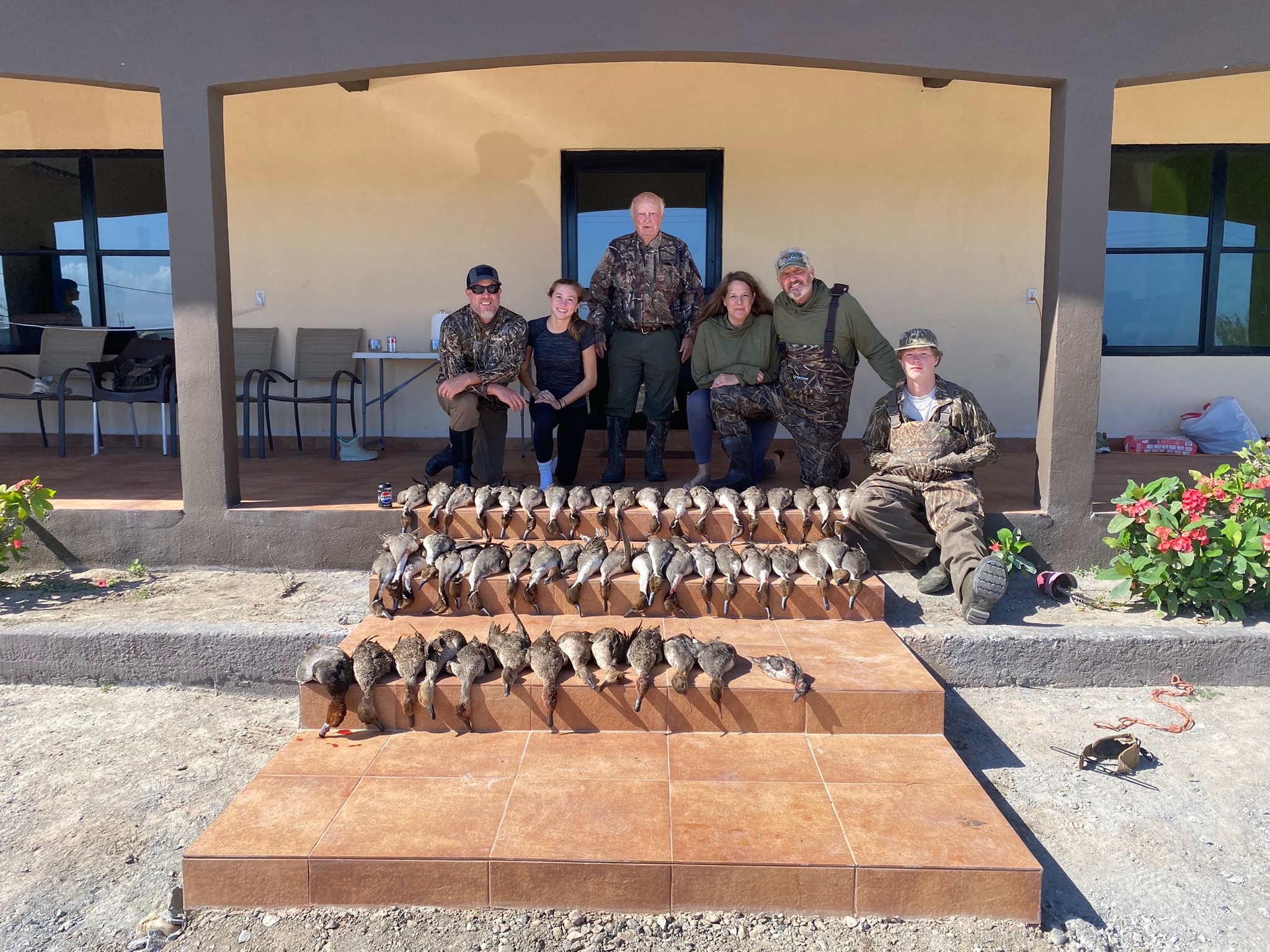 Group of hunters posing with a successful duck hunting catch, featuring numerous ducks displayed on steps in front of Palm Lodge, a hunting lodge on the Laguna Madre in Mexico.