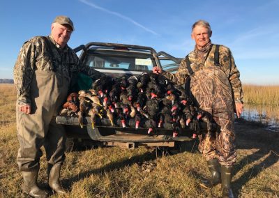 Hunters in camouflage standing beside a pickup truck loaded with harvested ducks, showcasing a successful waterfowl hunting trip at Estancia Santa Rita in Argentina.