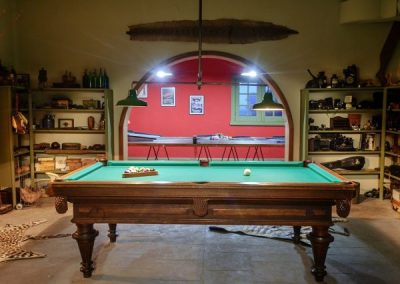 Billiards table in Estancia Santa Rita lodge, surrounded by vintage decor and a red wall, showcasing the rustic charm and leisure amenities available for guests.
