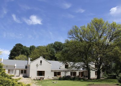 South African wingshooting lodge surrounded by trees and blue sky, featuring a spacious building designed for hunters and outdoor enthusiasts.