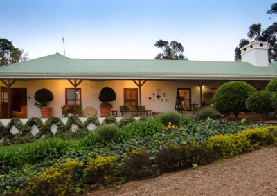 South African hunting lodge with a green roof, surrounded by landscaped gardens and trees, showcasing a welcoming atmosphere for wingshooting safaris.