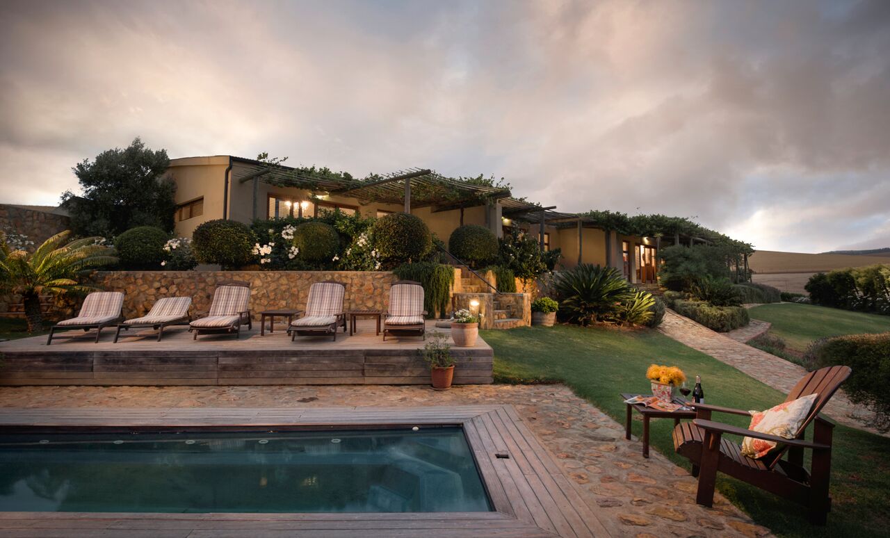 Luxury lodge exterior with poolside loungers, landscaped garden, and sunset sky, representing a premium accommodation option for hunting trips in South Africa.