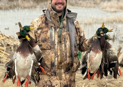 Hunter in camouflage holding multiple mallard ducks after a successful guided hunt in the Columbia Basin, showcasing the quality of Pacific Wings' hunting experience.