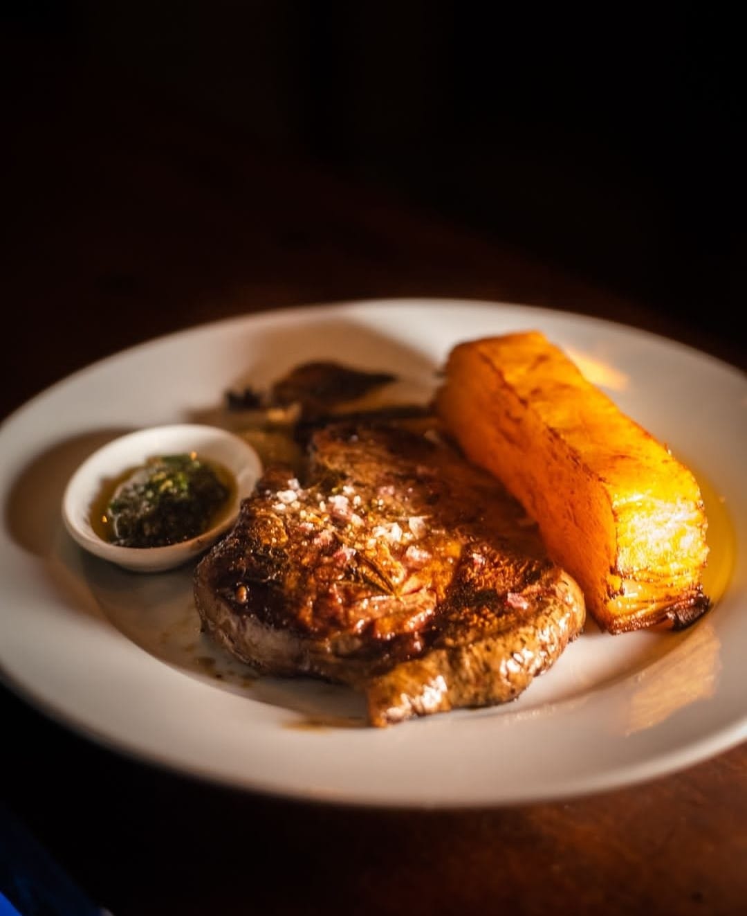 Grilled steak served with roasted plantains and a small bowl of green sauce, highlighting Uruguay's culinary offerings for hunting trip guests.