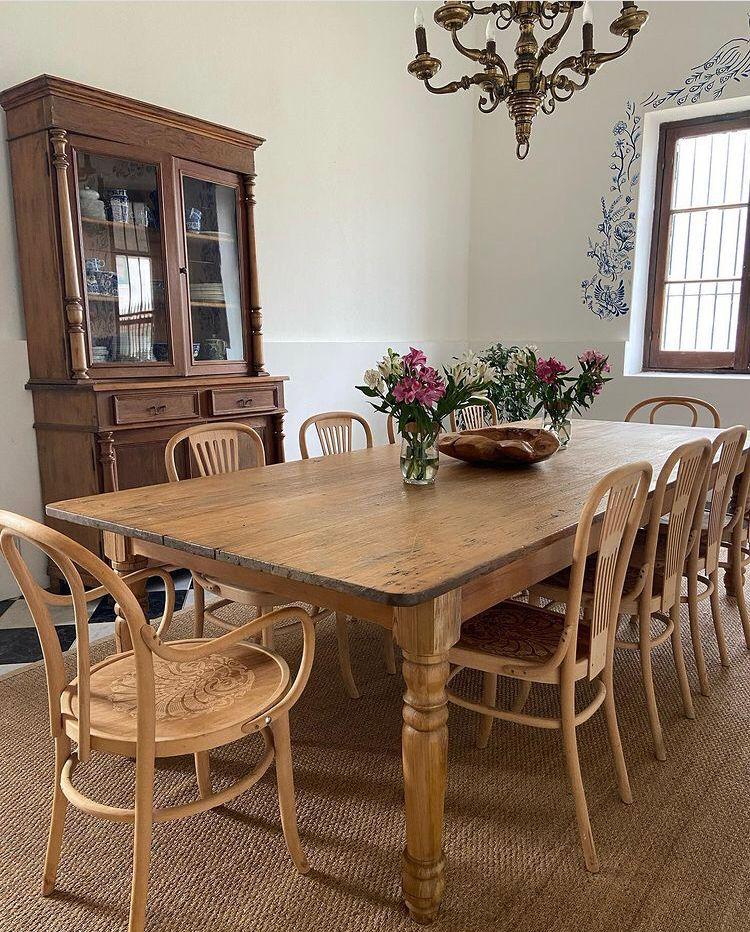 Elegant dining area with a wooden table, surrounded by light wooden chairs, a vase of flowers, and a vintage cabinet, reflecting a welcoming atmosphere for guests at a hunting lodge in Uruguay.