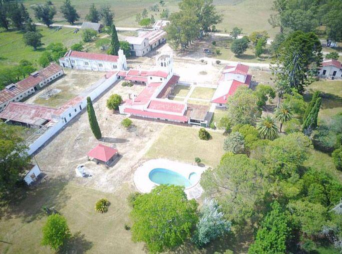 Aerial view of a hunting lodge in Uruguay featuring red-roofed buildings, a swimming pool, and lush greenery, highlighting the elegant hospitality for duck hunting and perdiz shooting experiences.