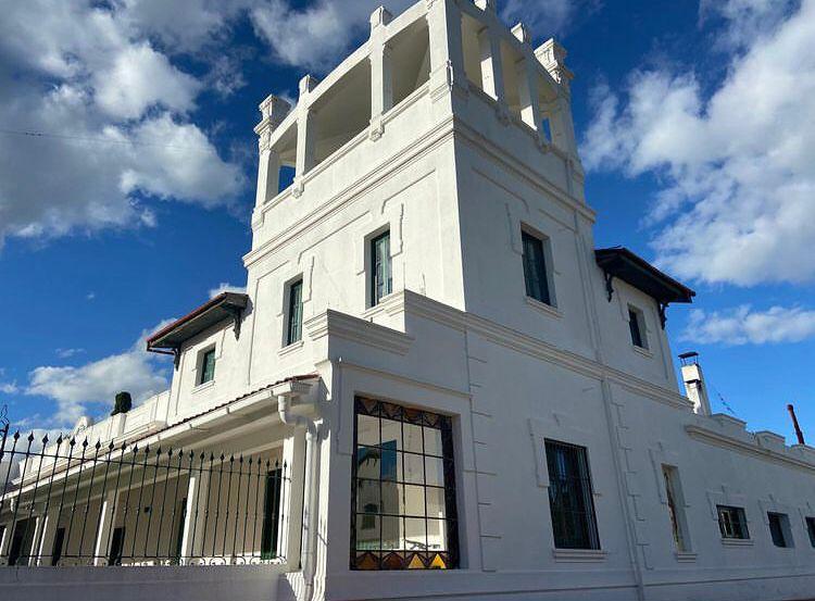 White architectural lodge with a tower and large windows, set against a blue sky with clouds, representing a luxurious hunting accommodation in Uruguay.