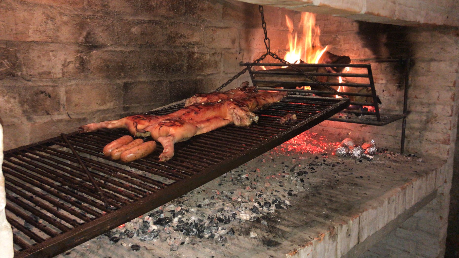 Wings-Uruguay-9 Grilled meats, including sausages and whole animals, cooking over an open flame in a traditional barbecue setting, highlighting the culinary experience for hunters in Uruguay.