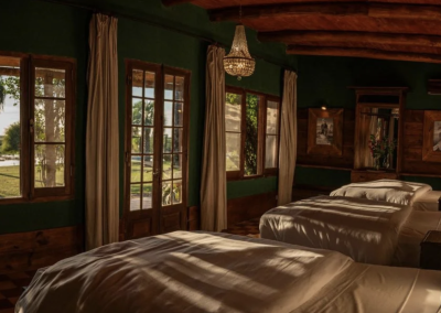 Elegant lodge interior at Don Joaquín River Lodge, Argentina, featuring beds and river view through windows.